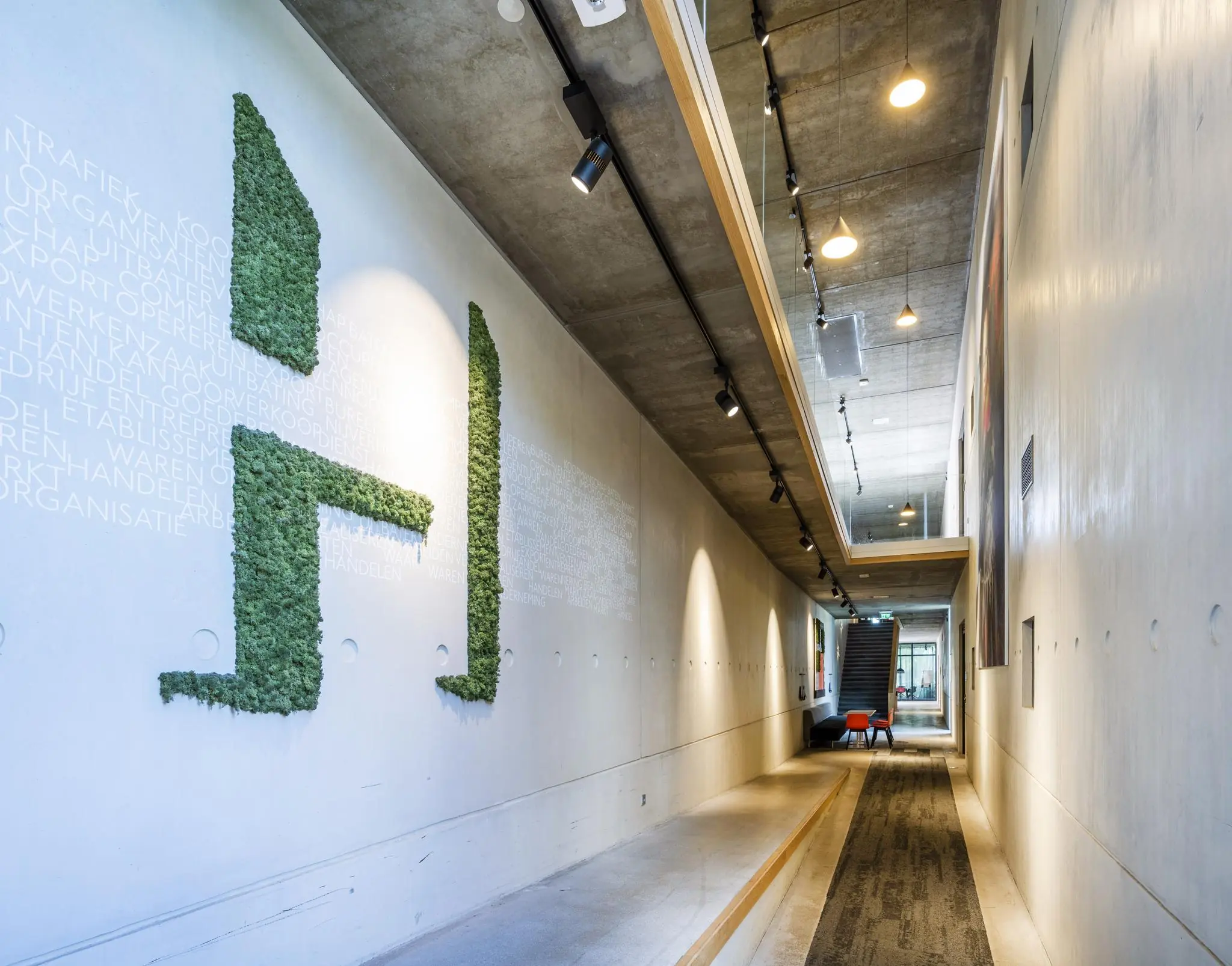 Moderne, betonnen gang in het Fred. Roeskestraat-gebouw met groene moswand in de vorm van een “H” en een trap aan het einde.